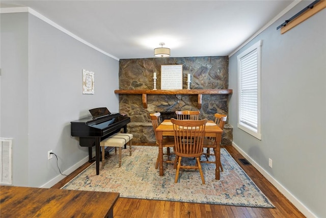 dining room with crown molding, visible vents, a stone fireplace, wood finished floors, and baseboards