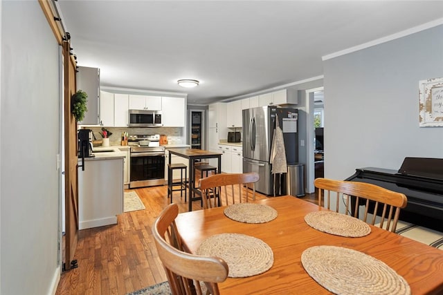 dining space with a barn door, light wood-type flooring, and crown molding