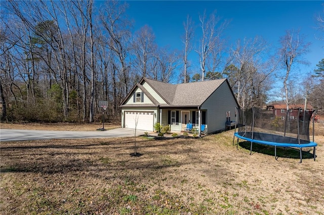 view of front of home with a trampoline, roof with shingles, covered porch, concrete driveway, and a front yard