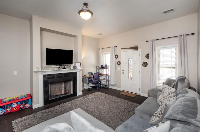 living area featuring a wealth of natural light, visible vents, a tile fireplace, and wood finished floors