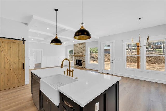 kitchen with beam ceiling, stainless steel dishwasher, a barn door, a sink, and light wood-type flooring