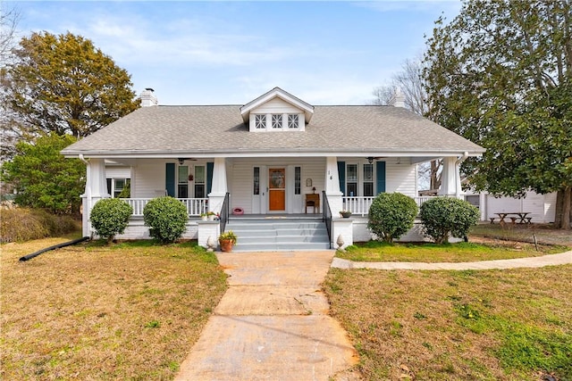 view of front of house with a porch, a front yard, roof with shingles, and a chimney