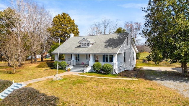 view of front of property featuring driveway, covered porch, a chimney, and a front lawn