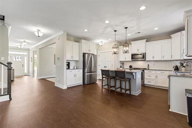 kitchen with appliances with stainless steel finishes, a kitchen bar, dark wood finished floors, and white cabinetry