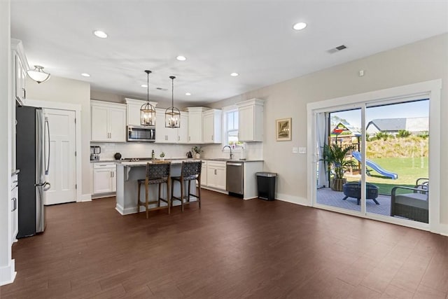 kitchen with dark wood-style flooring, visible vents, appliances with stainless steel finishes, a kitchen island, and a kitchen breakfast bar