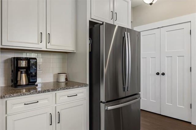 kitchen featuring tasteful backsplash, freestanding refrigerator, white cabinetry, and dark stone countertops