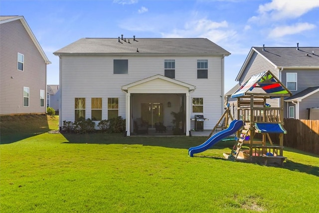 back of property with a sunroom, a playground, a lawn, and fence