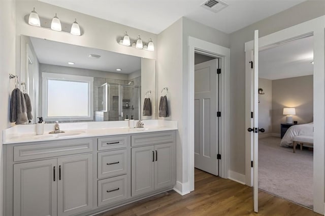 full bathroom featuring double vanity, a stall shower, visible vents, wood finished floors, and a sink