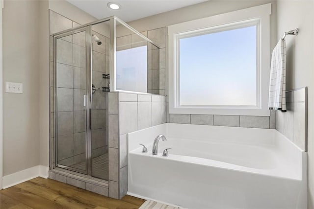 bathroom featuring a bath, a stall shower, baseboards, and wood finished floors