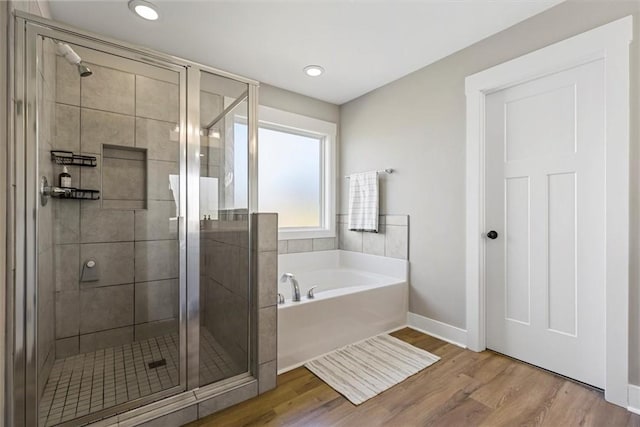 full bath featuring a stall shower, a garden tub, baseboards, and wood finished floors