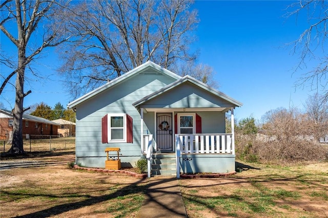 bungalow-style home with covered porch, a front yard, and fence