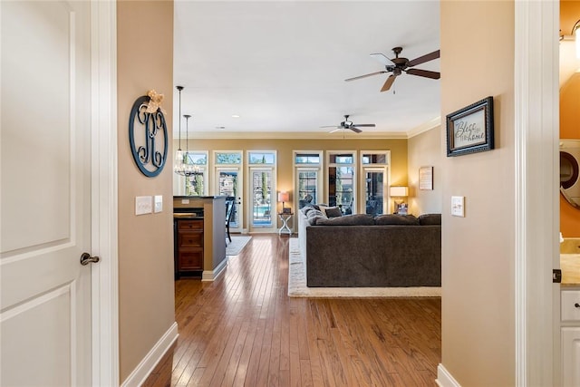 living area with hardwood / wood-style flooring, a ceiling fan, baseboards, ornamental molding, and washer / clothes dryer