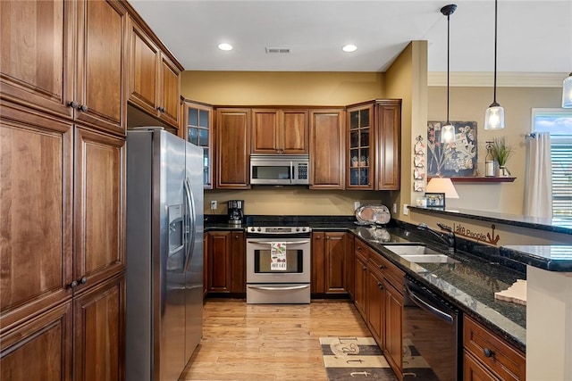 kitchen with a sink, appliances with stainless steel finishes, brown cabinets, light wood finished floors, and pendant lighting