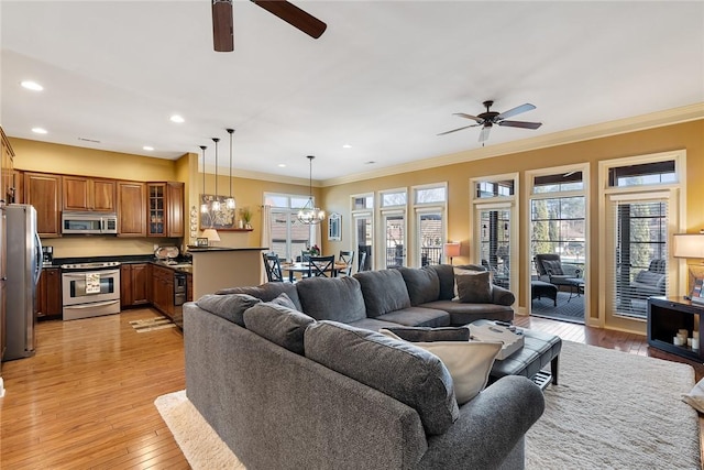 living room with light wood-type flooring, recessed lighting, ornamental molding, and ceiling fan with notable chandelier