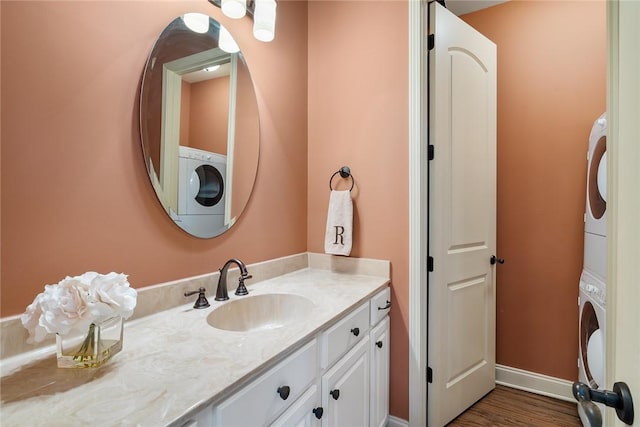 bathroom featuring stacked washer and dryer, wood finished floors, vanity, and baseboards