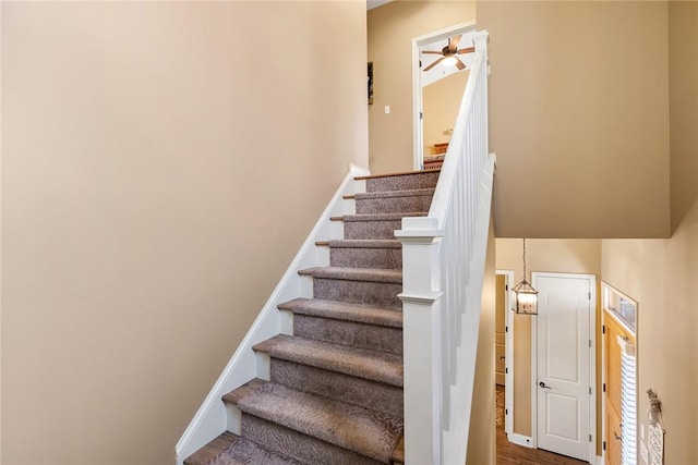 stairway with ceiling fan and baseboards