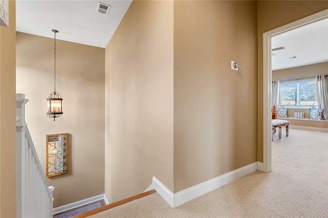 hall featuring carpet floors, visible vents, an upstairs landing, and baseboards