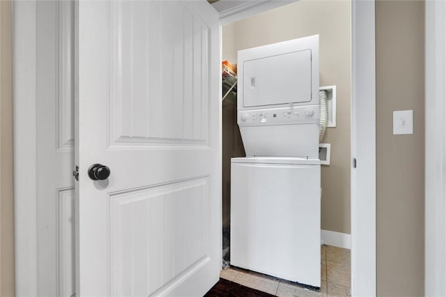 laundry room featuring stacked washer / drying machine, laundry area, tile patterned flooring, and baseboards