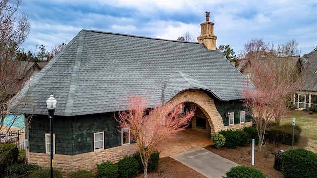 exterior space with stone siding, roof with shingles, and a chimney