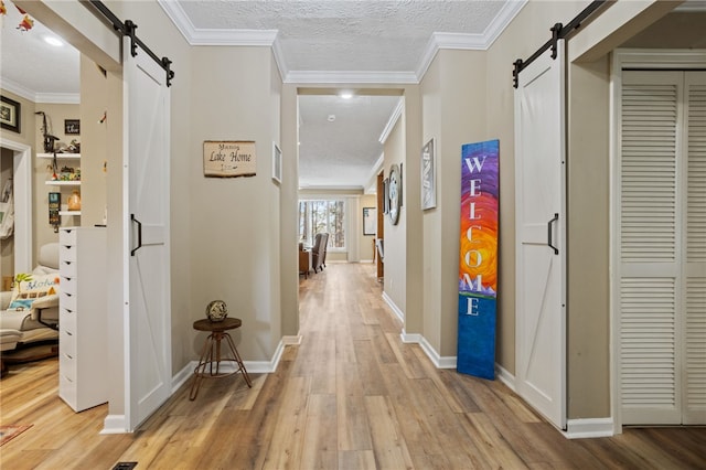 hall with a barn door, light wood-style flooring, and a textured ceiling