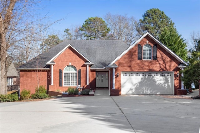 traditional-style home with a garage, roof with shingles, concrete driveway, and brick siding