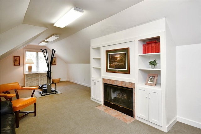 interior space featuring built in shelves, light carpet, baseboards, vaulted ceiling, and a tiled fireplace