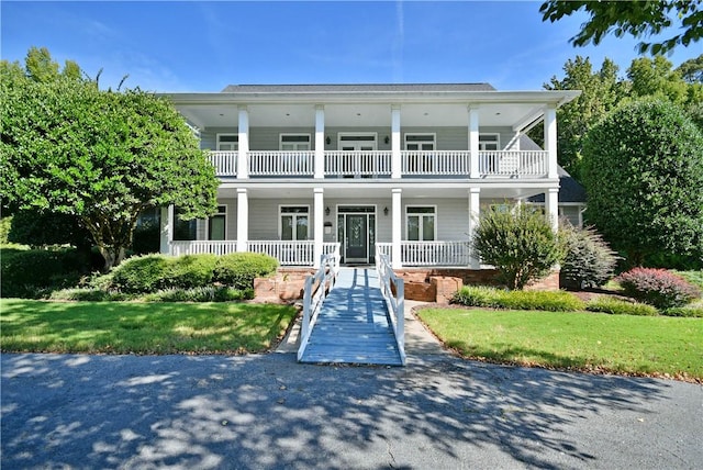 greek revival inspired property featuring a balcony, covered porch, and a front yard