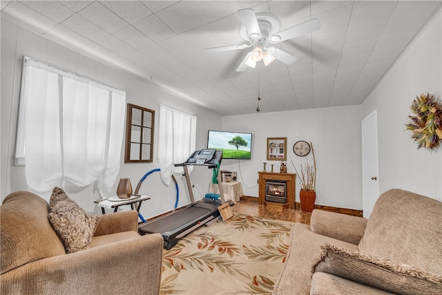 living area with a warm lit fireplace, ceiling fan, and baseboards