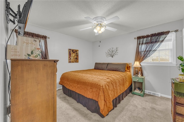 bedroom with a textured ceiling, ceiling fan, light colored carpet, visible vents, and baseboards