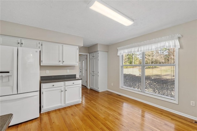 kitchen featuring white fridge with ice dispenser, dark countertops, light wood-type flooring, and white cabinetry