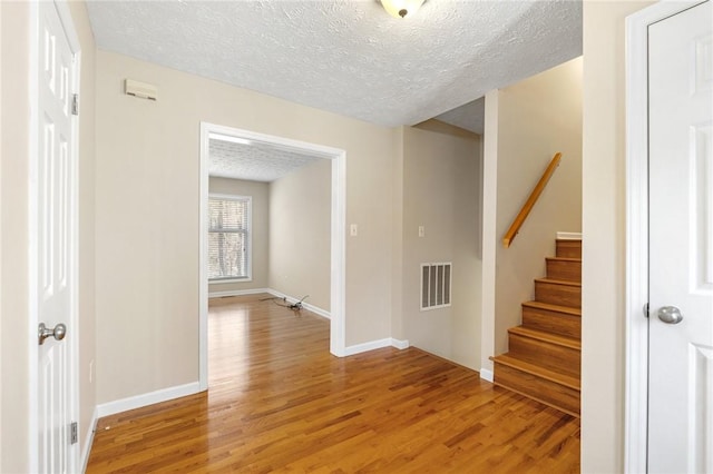 corridor featuring stairway, light wood-type flooring, visible vents, and a textured ceiling