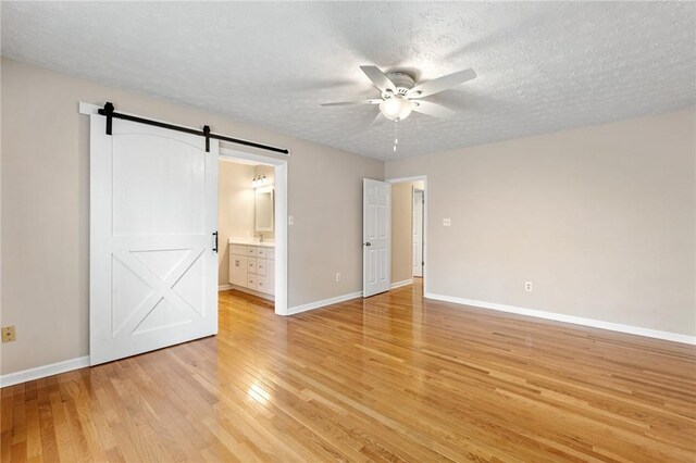 unfurnished bedroom with a barn door, baseboards, light wood-style flooring, ensuite bathroom, and a textured ceiling