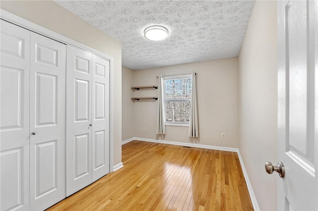 unfurnished bedroom with light wood finished floors, a closet, visible vents, a textured ceiling, and baseboards