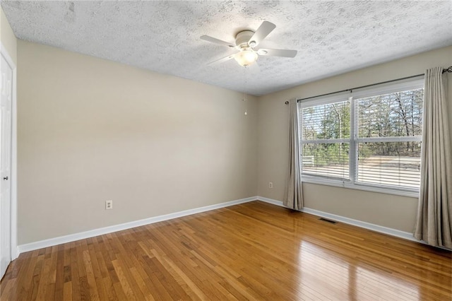 spare room with wood-type flooring, a textured ceiling, visible vents, and baseboards