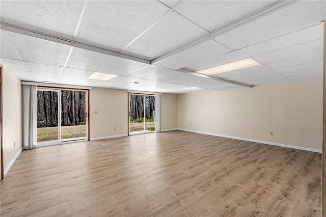 spare room featuring light wood-style floors, a drop ceiling, and baseboards