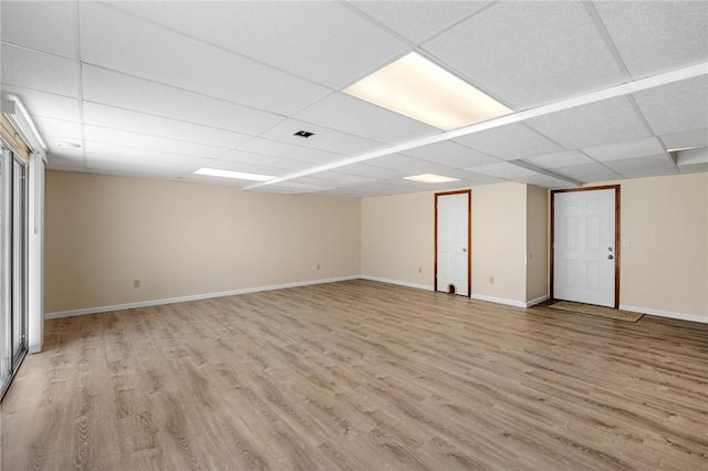 finished below grade area featuring visible vents, baseboards, a drop ceiling, and wood finished floors