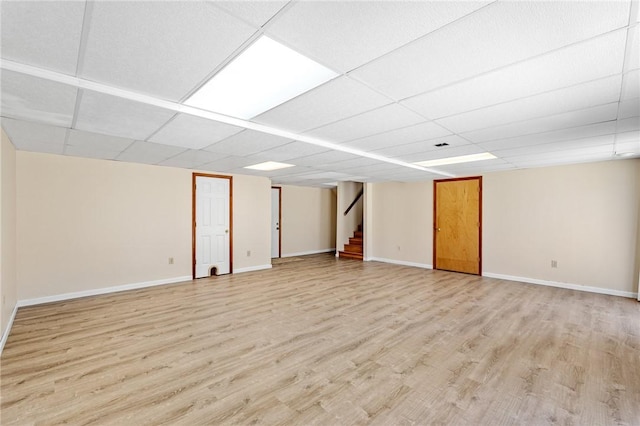 finished basement with light wood-style floors, a paneled ceiling, stairway, and baseboards