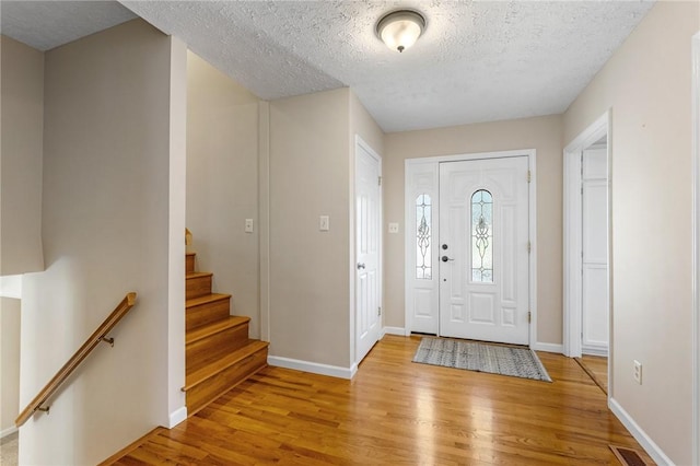 entryway with a textured ceiling, light wood-type flooring, visible vents, and baseboards