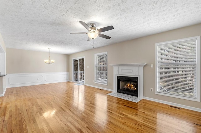 unfurnished living room featuring visible vents, a fireplace with flush hearth, light wood-style floors, a textured ceiling, and ceiling fan with notable chandelier