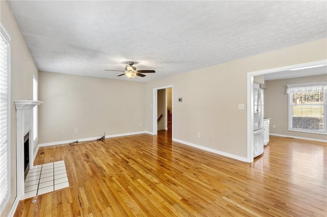 unfurnished living room featuring light wood-style floors, a fireplace with flush hearth, baseboards, and a textured ceiling