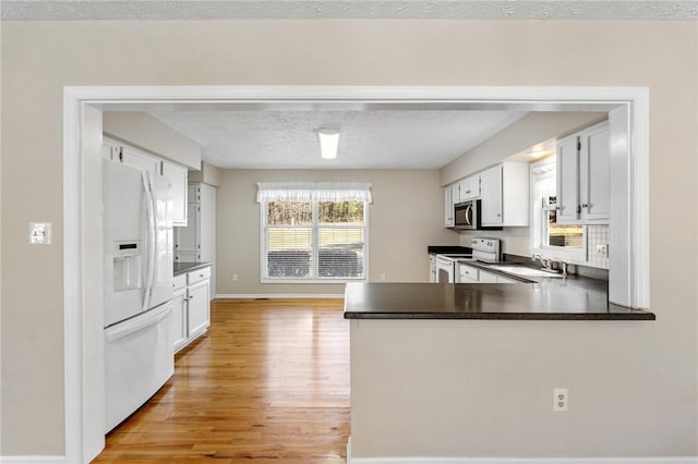 kitchen featuring white appliances, dark countertops, a peninsula, a textured ceiling, and light wood-style floors