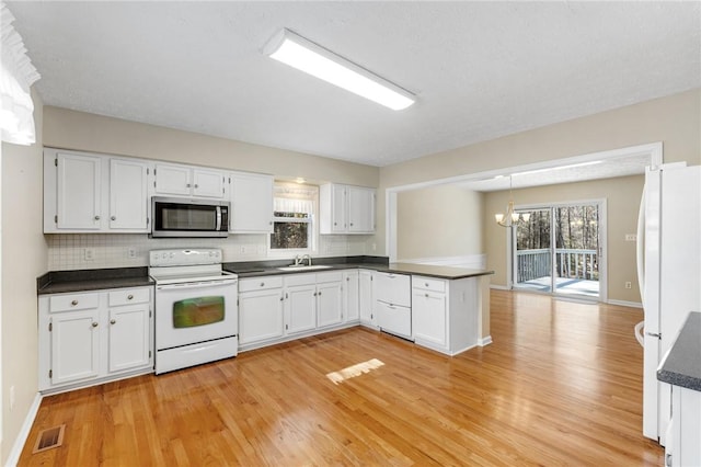 kitchen with white appliances, visible vents, dark countertops, a peninsula, and a sink