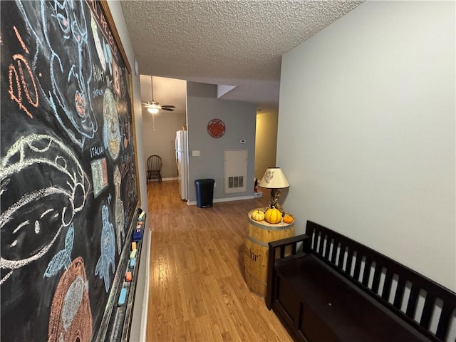 hall with baseboards, visible vents, light wood-style flooring, and a textured ceiling