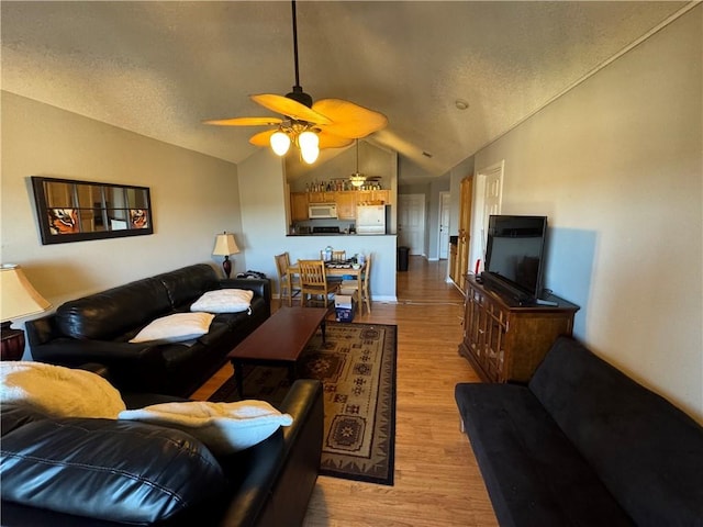 living room with vaulted ceiling, ceiling fan, a textured ceiling, and light wood-style floors