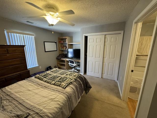 bedroom with a closet, light colored carpet, visible vents, a ceiling fan, and a textured ceiling