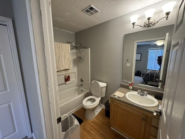 full bath with a textured ceiling, toilet, wood finished floors, vanity, and visible vents