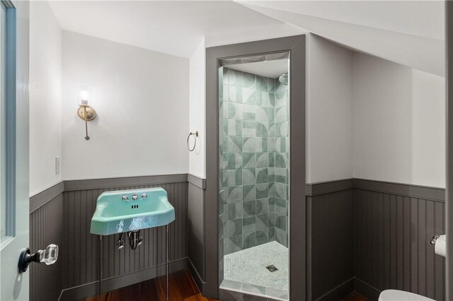 bathroom with a tile shower, wood finished floors, and wainscoting