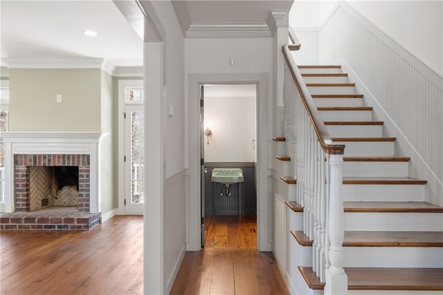 staircase featuring ornamental molding, a fireplace, hardwood / wood-style flooring, and recessed lighting