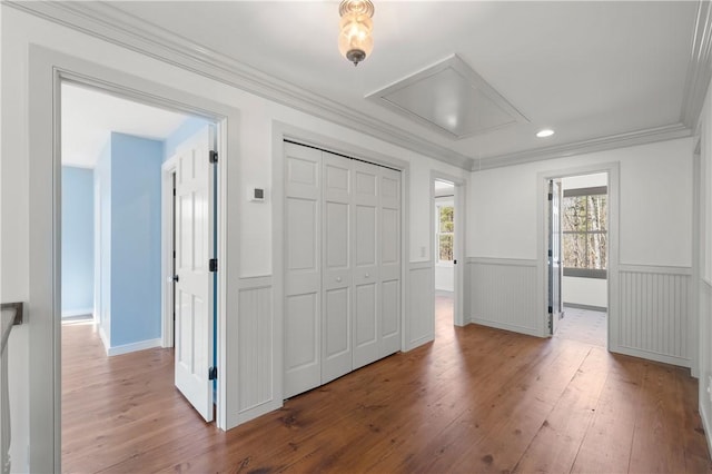 unfurnished bedroom featuring hardwood / wood-style flooring, a closet, wainscoting, attic access, and crown molding