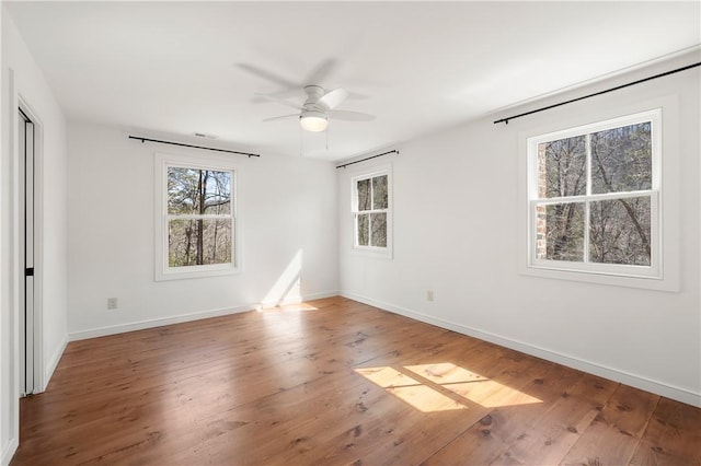 unfurnished bedroom featuring hardwood / wood-style floors, multiple windows, a ceiling fan, and baseboards